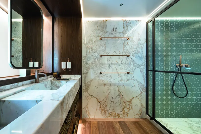 A guest bathroom, book-matched marble on one side and a patterned-tile shower behind glass on the other.