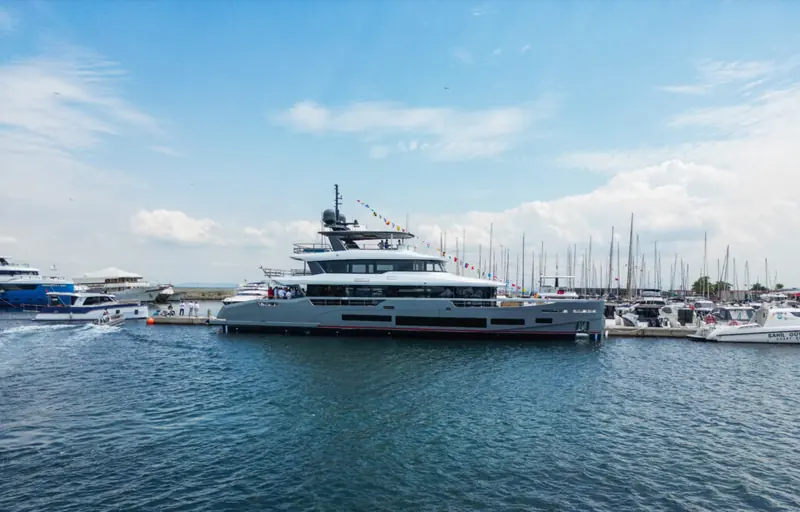 Broadside at the quay on launch day, the marina's sailboats behind her - the flagship left an inland build hall for this coastal yard.