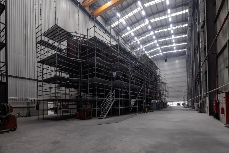 The hull sits mid-build in Sirena's construction hall, dwarfed by the shed's cranes and lighting rig.