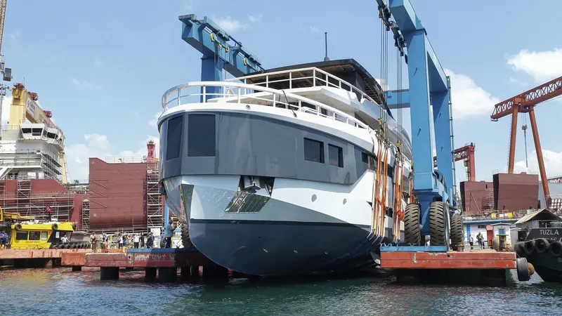 Lointaine held on slings at the bow as the travel lift lowers her toward the water at Soyaslan Marine's Turkish yard, 13 August 2026.