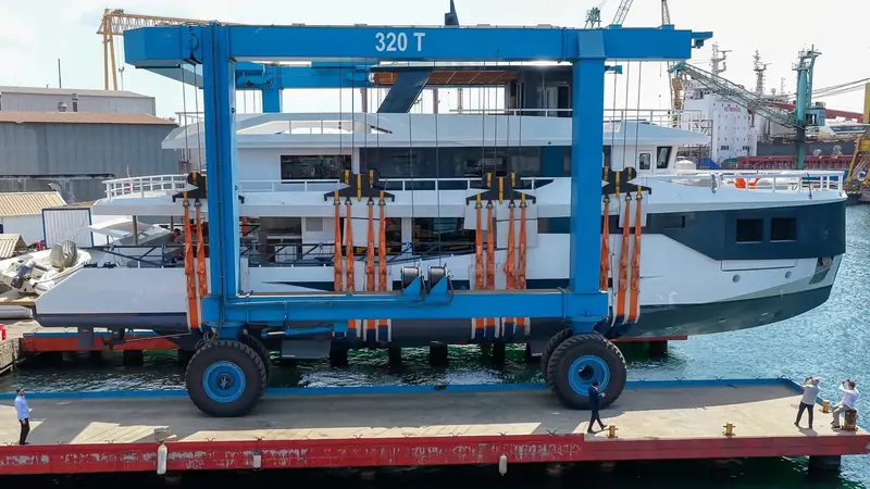 The transporter carries her toward the water's edge, flanked by the gantry crane that will have handled the hull sections during the build.