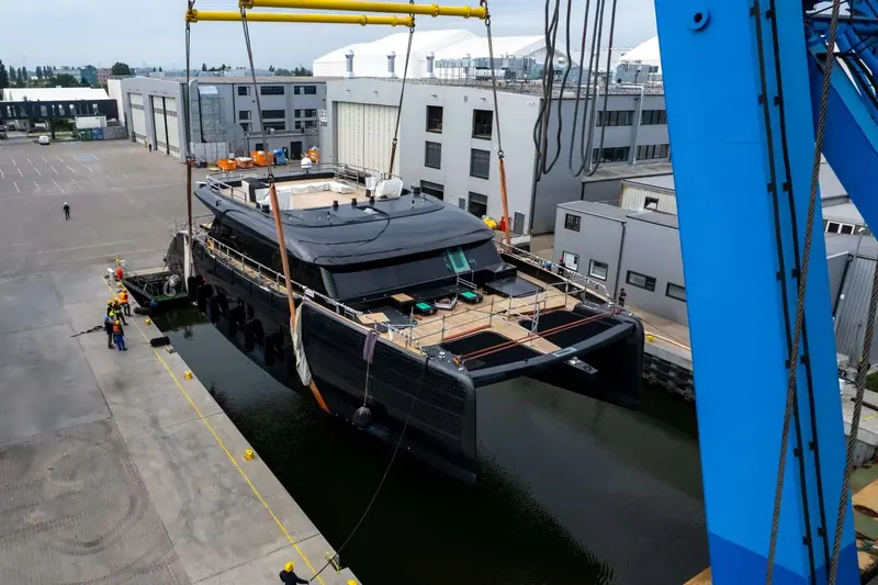The first Sunreef 100 Eco is lifted from the shipyard basin at Gdansk in June 2026, her hull still wrapped for the move.