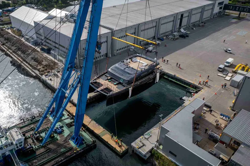 The hull touches the water for the first time, shipyard staff watching from the quay at Sunreef's Gdansk yard.