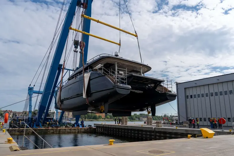 The hull swings from the mobile crane moments before touching down, the solar-panelled deck visible under its wrap.