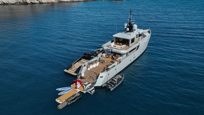 Moonshot at anchor off a rocky coastline, her stern-mounted water-toy garage and tender deployed.