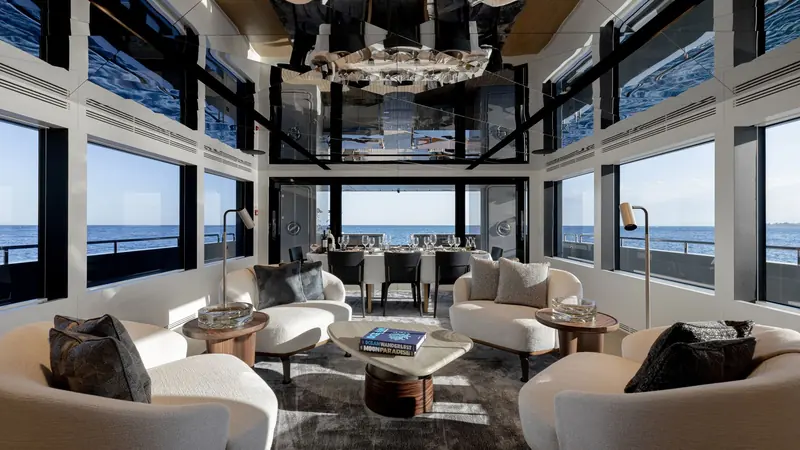 The main saloon's mirrored ceiling and full-height windows open onto the dining table and a wraparound lounge.
