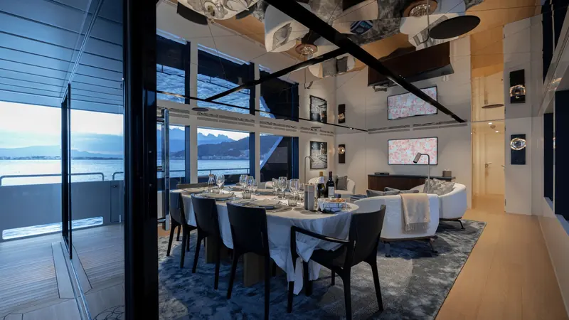 The formal dining table set beneath a mirrored, beamed ceiling, with the aft deck visible through full-height glass.