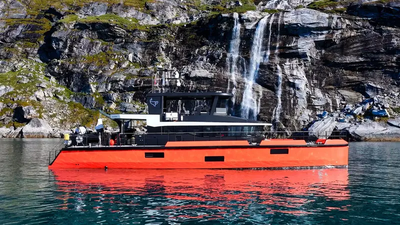 Vanguard anchored below a Greenland waterfall. Her red hull and low-profile black superstructure are shared across the whole Naval Yachts XPM range.