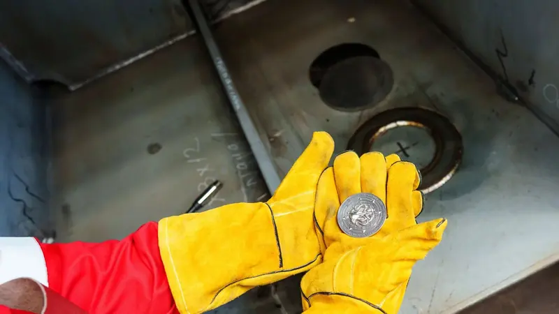 A yard worker sets the traditional coin against the keel plate before it is welded in, the ritual marker of a hull's first steel.