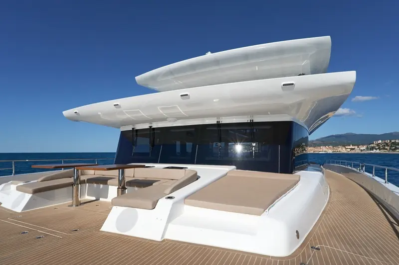 Atraversia's flybridge sun deck under way off Imperia, the raked hardtop that carries her 54-panel solar array visible above the aft saloon glazing.