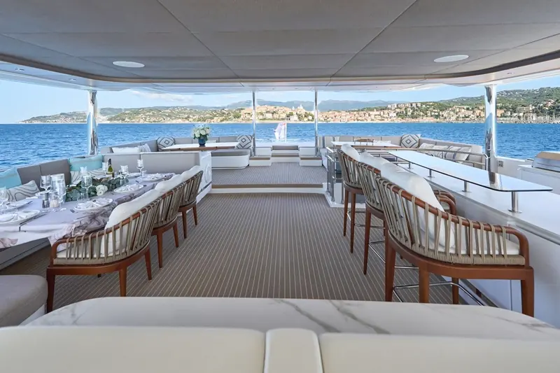 The aft cockpit dining table laid for guests, with the town of Imperia and Liguria's coastal hills across the water astern.
