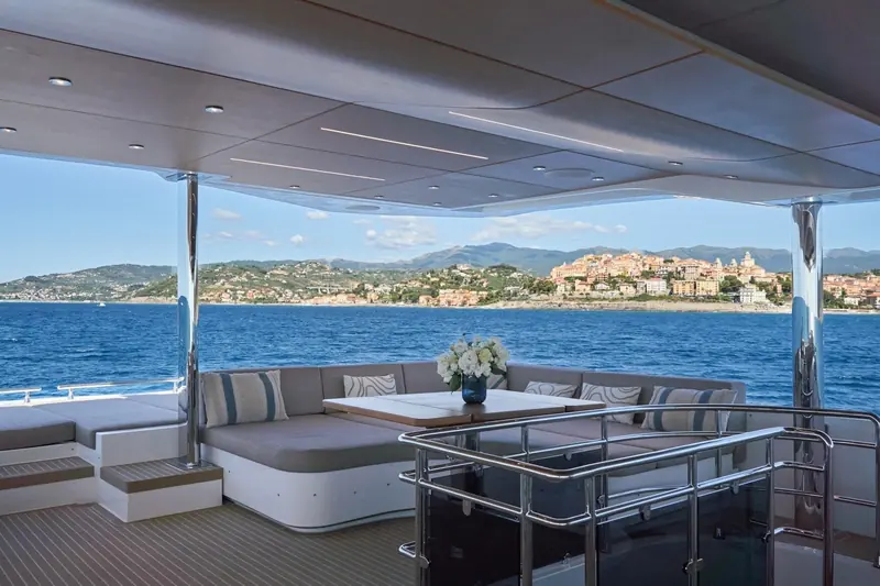 A second view of the aft deck table, Imperia's old town visible across the bay, on the same stretch of Ligurian coast the yacht was photographed for her current listing.