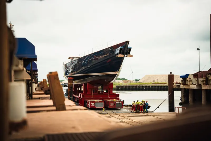 Alongside the quay, riggers prepare lines beneath a hull with no sea-strainers for engine cooling and no exhaust ports - there is no combustion engine and no generator aboard to need them.