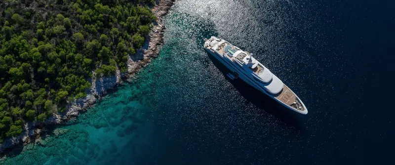 An aerial view of Casa entering a rocky, turquoise-water anchorage off Mallorca.