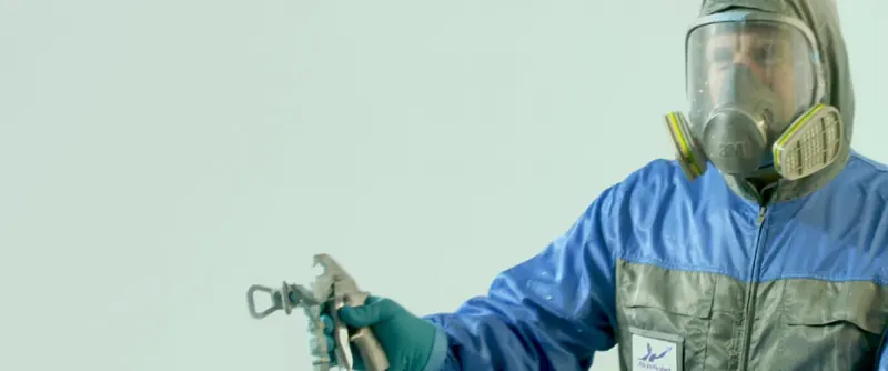 An AkzoNobel applicator in full spray gear working an Awlgrip topcoat onto a hull.