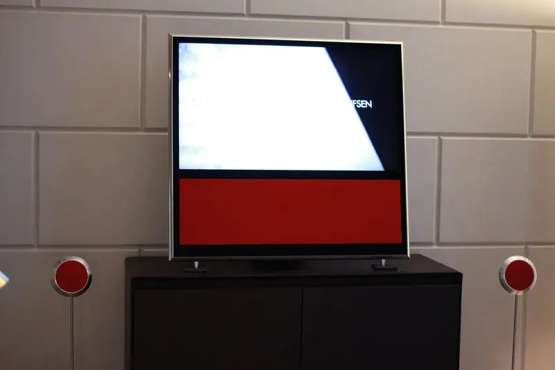 Two red BeoLab disc speakers flank a Bang & Olufsen flat screen on a dark cabinet.