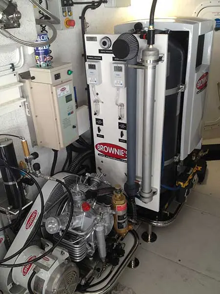A compressor block feeds a tall Brownie's nitrox membrane column built into a dive locker, cylinders and hose reels crowded into the space around it.