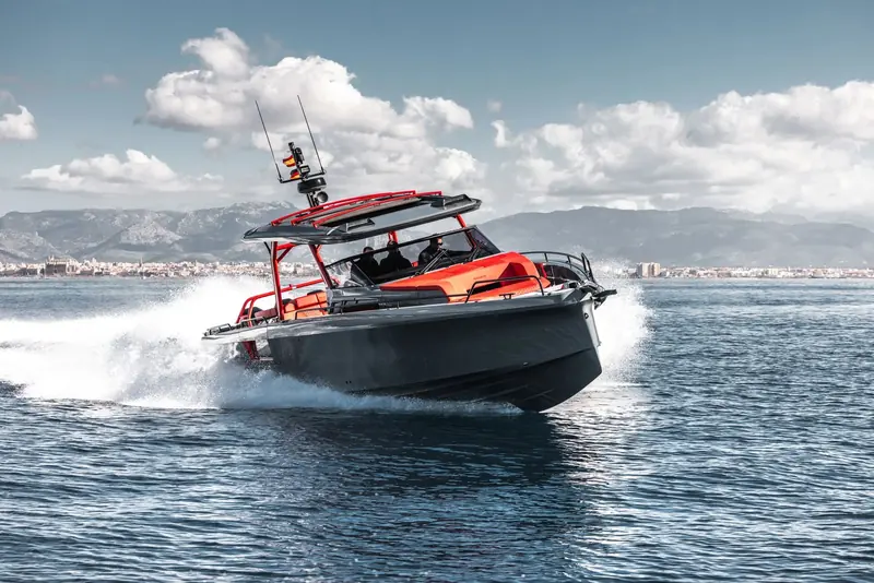 A Shadow 1200 XT Black Ops in red and grey runs bow-up off Palma de Mallorca, the cathedral skyline behind her, three people aboard under the roll bar and hardtop.