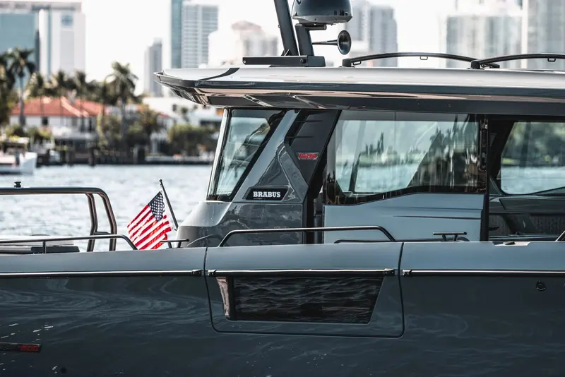 A close detail of the Shadow 1500's carbon hardtop and BRABUS door badge, a US flag at the transom rail and the Florida waterfront skyline soft behind the glass.