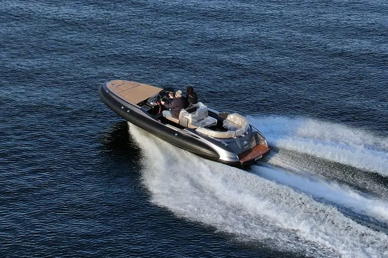 A jet tender runs hard across open water with two people aboard and the seating still under protective wrap.