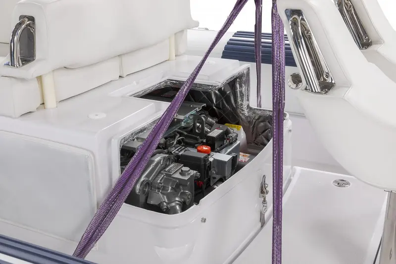 The engine hatch stands open in the cockpit of a white jet tender, showing the engine and the foil lined underside of the lid. Purple lifting strops are rigged across the boat and over the moulded seating.