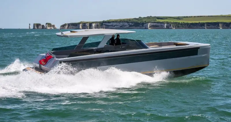Off a green headland, a grey open tender pushes a clean bow wave with two people aboard.