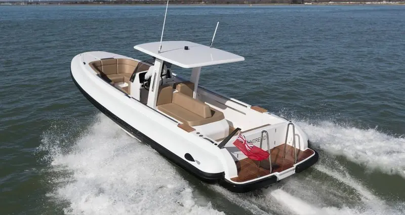 Teak decking and a slim white hardtop mark a rigid inflatable tender planing across cold open water.