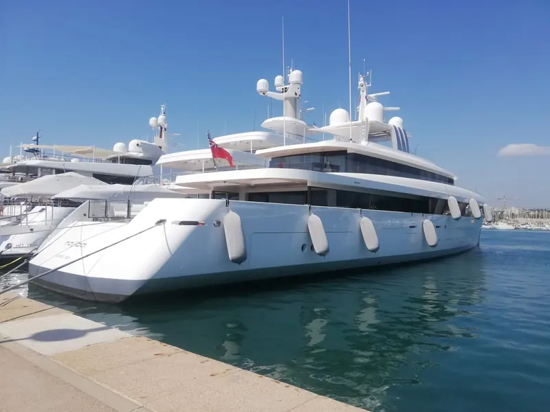 Fendertex fenders in a pale hull-matched cover hang along the bow of the superyacht Najiba in a Mediterranean marina, color-coordinated rather than the usual white or black.