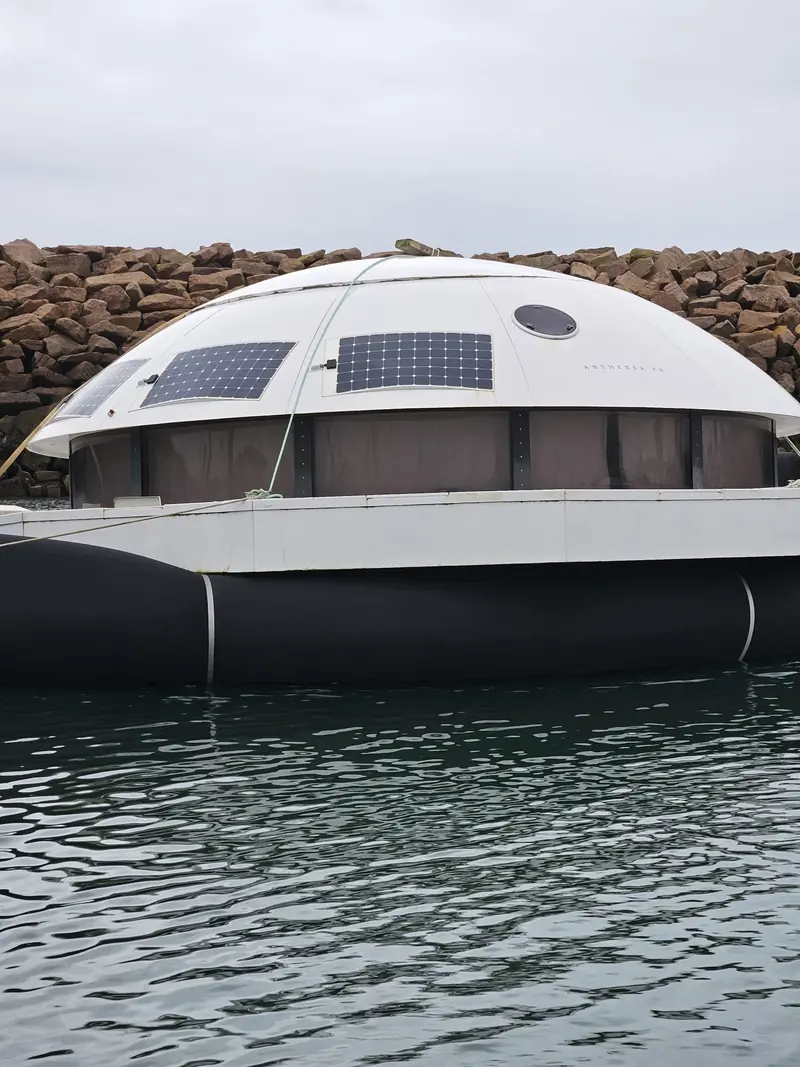 A large black Fendertex textile flotation collar supports the Anthenea floating solar-powered pod off a breakwater, an example of the maker's custom projects beyond standard boat fenders.