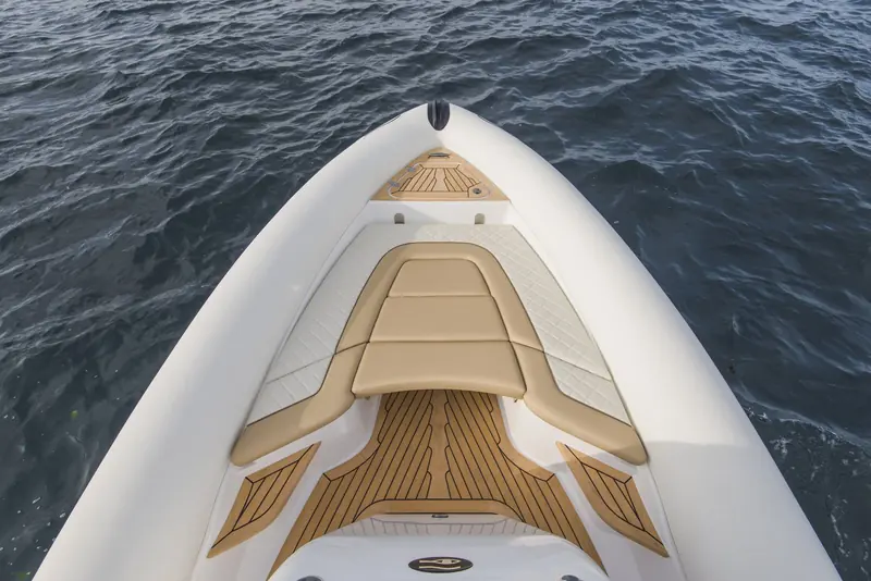 The bow sunpad area of a Ribeye Prime 821 finished in Flexiteek teak with black caulking, showing the mitred plank pattern fitted tight around the seat bolsters and a deck hatch.