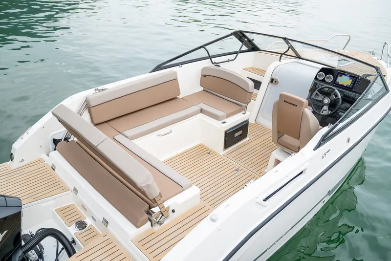 A Quicksilver Activ 675 cockpit at rest on a lake, its sole and side decks laid in Flexiteek scrubbed-finish decking with black caulking around the helm, seating and engine well.