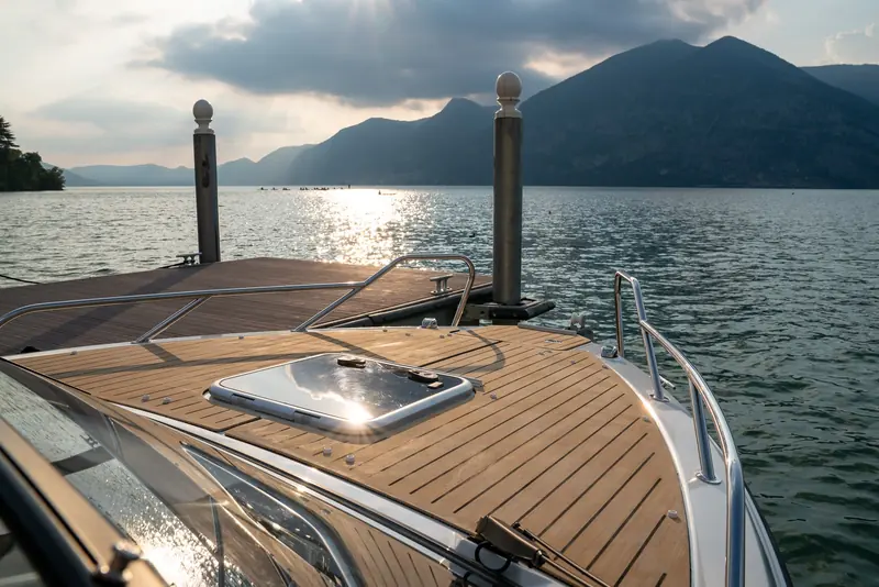 Flexiteek decking on a motor yacht's foredeck at a lake mooring in evening light, laid in straight planks around a deck hatch with visible plank-to-plank seams.