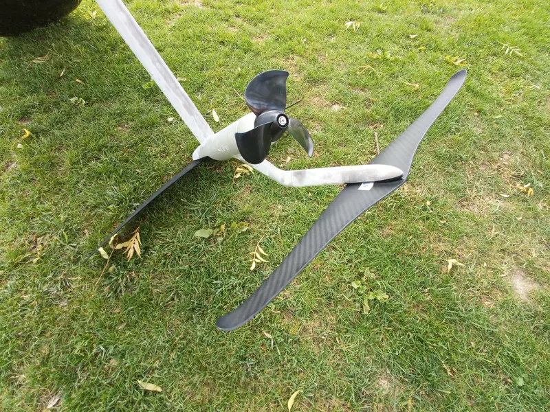 The drive unit off the board and set on grass: front wing, mast and the rear propeller pod, its housing stamped FLITE, with the carbon stabiliser wing crossed beneath it. This is the hardware that stays underwater and out of sight while riding.