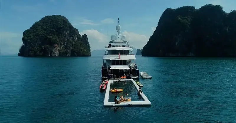 A superyacht lies between limestone karsts with an inflatable sea pool and toys rigged off her stern.