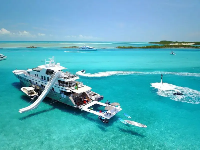 In pale Bahamian shallows a motor yacht sits at anchor with an inflatable slide and platform rigged aft.