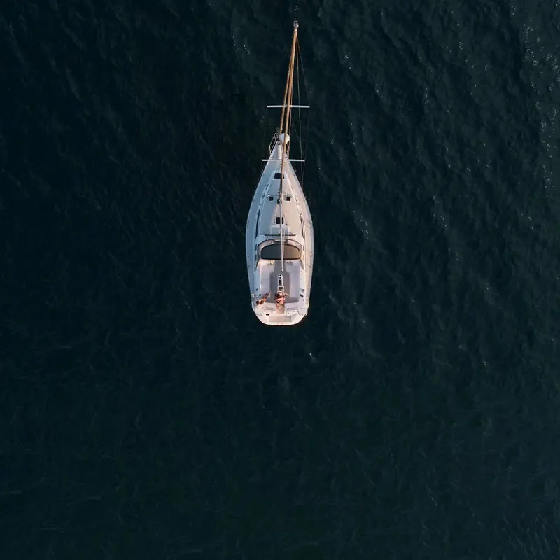 A sailing yacht held on a steady course at anchor, seen from directly overhead: the kind of hands-off heading-keeping a marine autopilot is built to do underway.