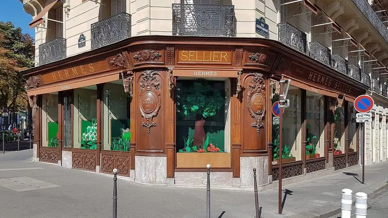 Gilded lettering reads Hermes Sellier above corner windows dressed with cut paper leaves and flowers.