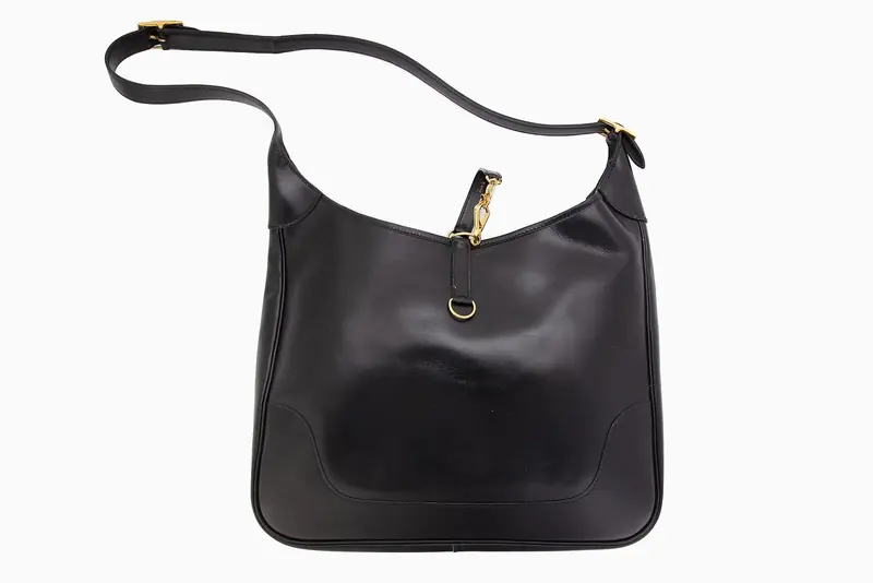 A black box-leather Trim shoulder bag with gold-tone hardware - the trigger-snap clasp on the strap is a Hermes equestrian detail, carried over from the tack room into the handbag line.