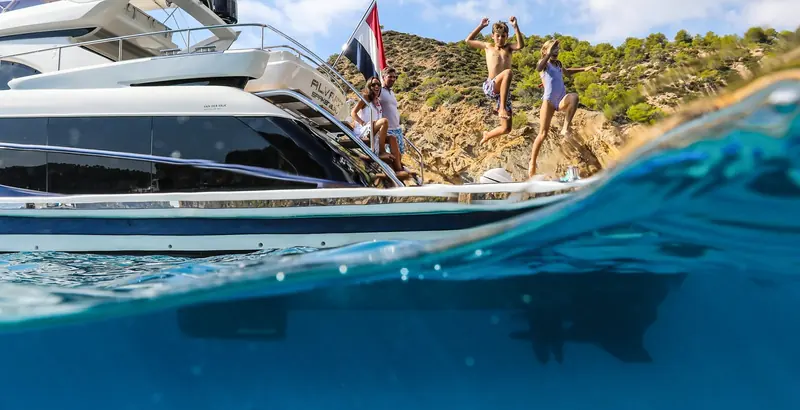 A family jumps from a Van der Valk motoryacht at anchor in a quiet cove, the at-rest condition Humphree's fin stabilisers are built to calm without a hydraulic pump or a running generator.