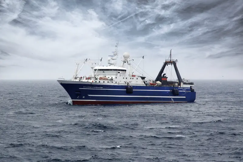 A deep-sea factory trawler under a grey Arctic sky, a small radome visible near her mast, from Intellian's own material on VSAT for the commercial fishing fleet.