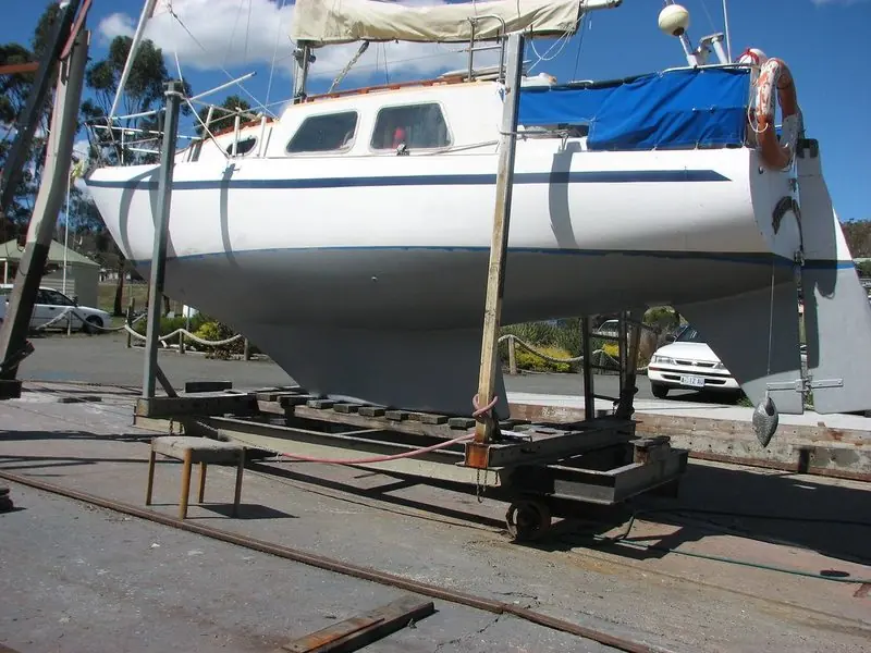 A sailboat cradled ashore mid-way through hull preparation, with a grey bonding coat applied ahead of the antifouling topcoats.