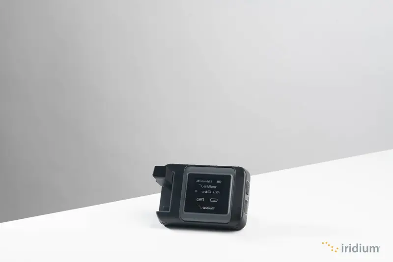The Iridium GO satellite hotspot in a studio product shot, showing the compact, pocket-sized form factor crews carry as a backup to a fixed terminal.