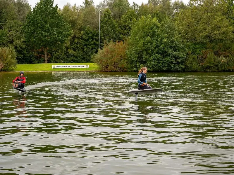 Two riders cross the Messesee at Interboot, one lifted clear of the water on a hydrofoil.