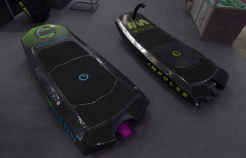 A Bizon and an Impulse hull side by side on a show-stand floor, the carbon deck grip, jet nozzle and fuel cap visible with the top cowling off.