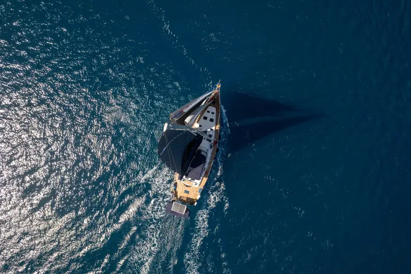 A sailing yacht seen from directly overhead, under short sail and drawing a long wake, equipped with Lewmar deck hardware.