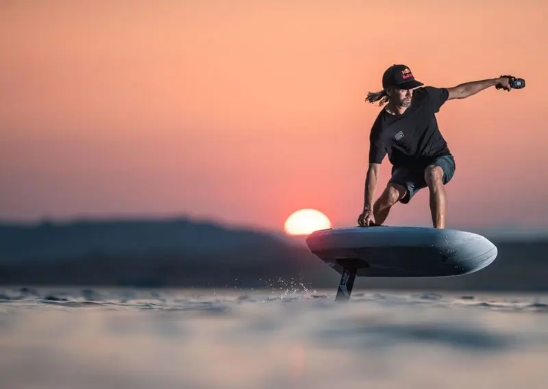 A rider carves a Lift eFoil across flat water as the sun drops to the horizon.