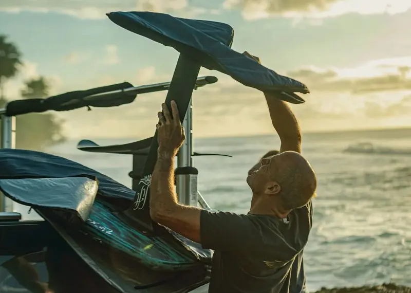 Loading up at the end of the day, a man lifts a covered board and its foil onto a boat rack.