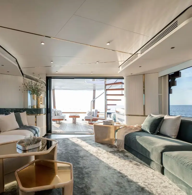 A saloon aboard a motor yacht with a green velvet sofa and a deep pale carpet, the aft doors open to the cockpit and a spiral stair rising beyond them.