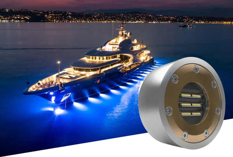 A superyacht lit blue along the waterline at dusk, inset with a Lumishore weld-in underwater light module for a permanently installed housing.