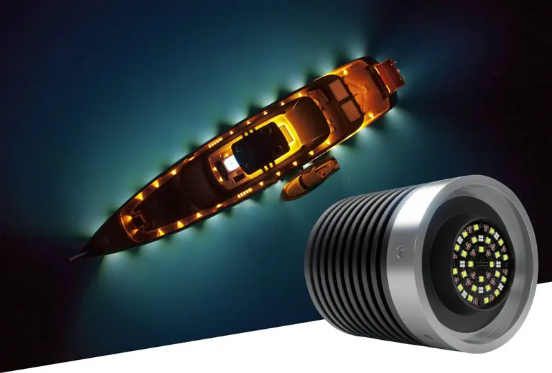 A superyacht seen from directly overhead at night under amber deck lighting, inset with a studio shot of a Lumishore retrofit underwater light.